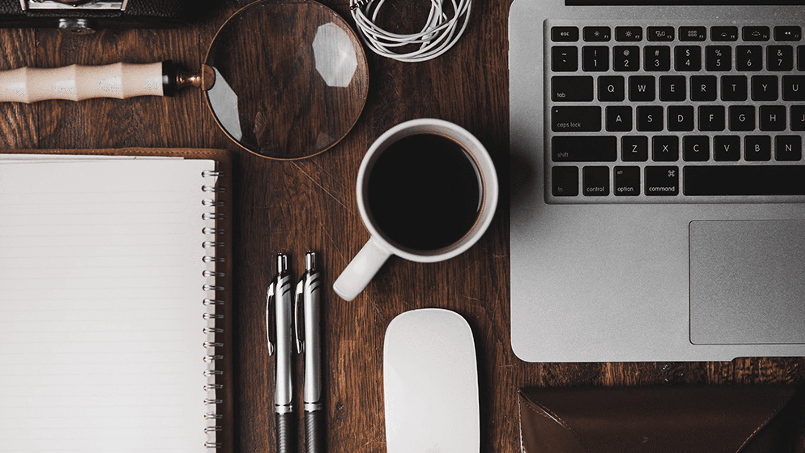 Desk with laptop, coffee mug, pens, mouse, and magnifying glass