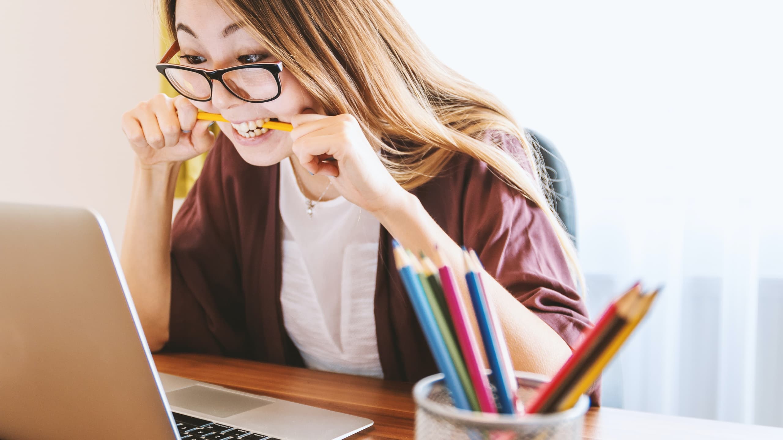Woman biting pencil while staring at laptop
