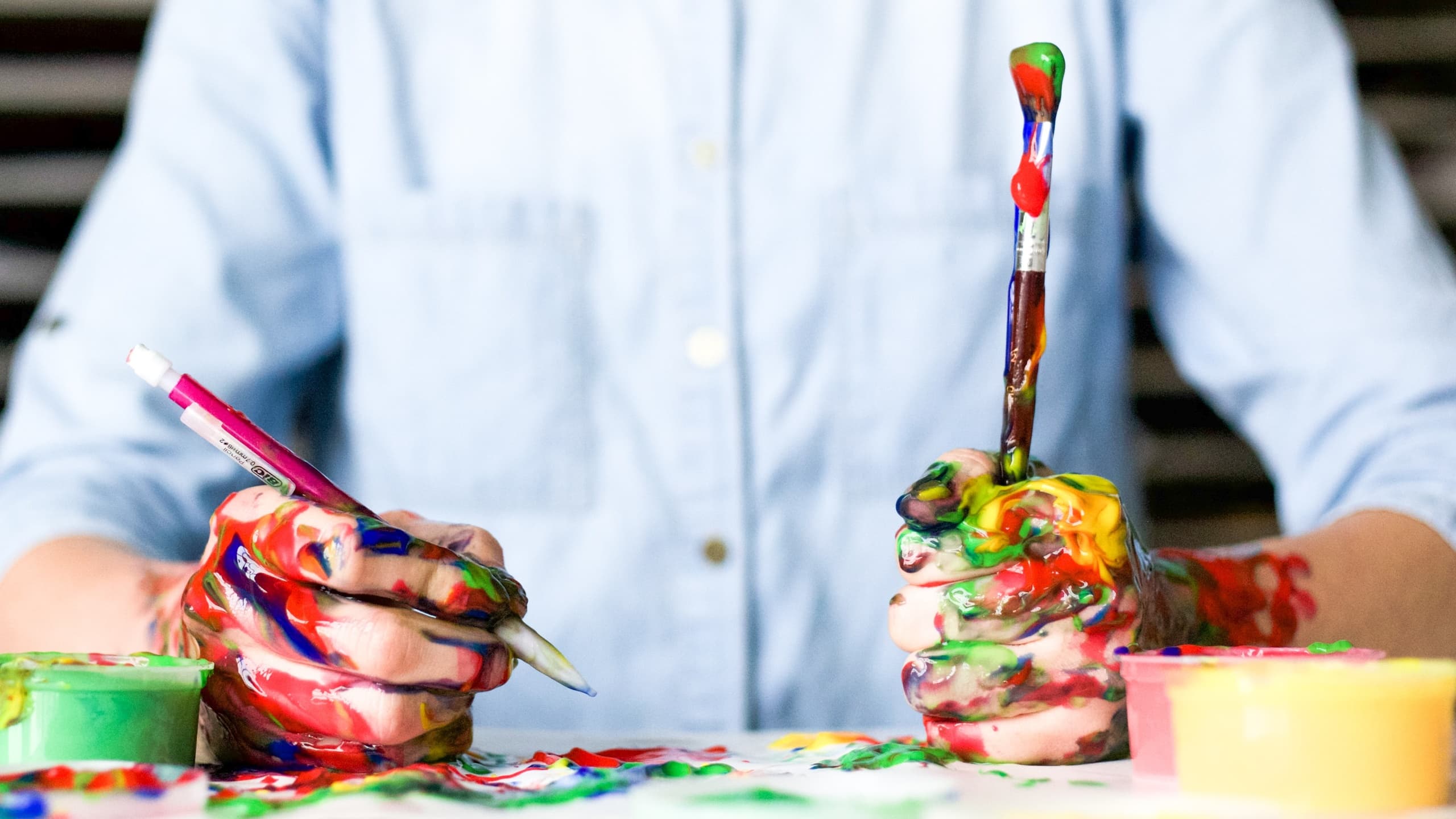 Man holding two paintbrushes with pain on his hands