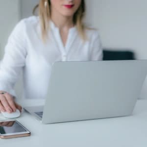 A woman is working at her computer.  Her phone is on the desk by her