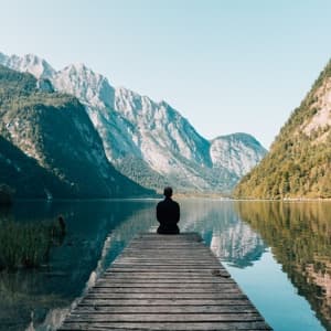 Man meditating while seated overlooking lake in mountainous region